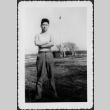 Man standing in field, flag pole in background (ddr-densho-434-401)