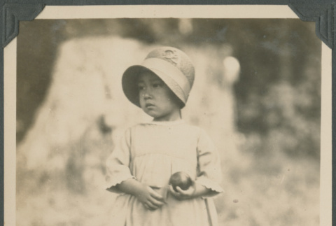 Girl holding an apple standing in field (ddr-densho-483-521)