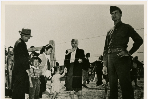 Family greeting older woman behind barbed wire with guards (ddr-densho-122-725)