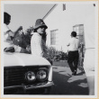 Woman in hat leaning on car in driveway (ddr-densho-522-95)