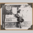Man poses next to a perfume sign (ddr-densho-542-59)