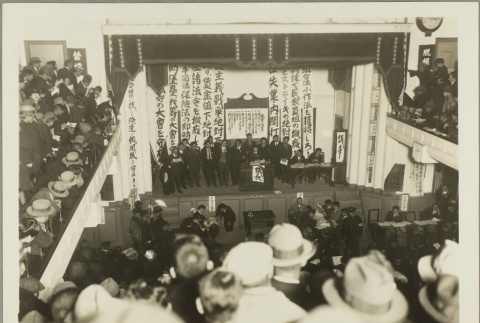 Men standing on stage in a crowded event hall (ddr-njpa-13-1442)