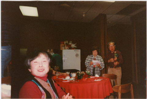 Tomoye and Henri Takahashi standing by table with gifts, woman in foreground (ddr-densho-426-1298)