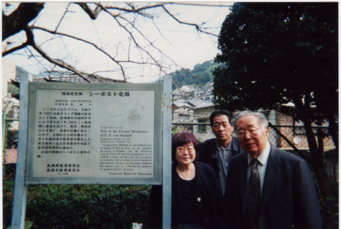 Tomoye, Norman and Henri Takahashi standing by sign for Siebold Residence, Nagasaki (ddr-densho-426-532)