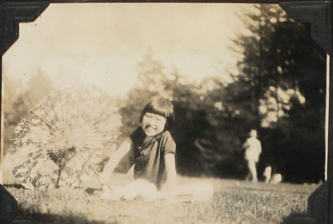 Girl sitting on grass with paper parasol (ddr-densho-423-497)