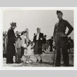 Guard standing next to a family visiting though a barbed wire fence (ddr-densho-259-725)