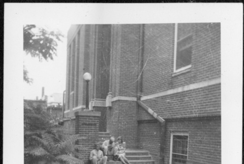 Two men and a woman sitting on stairs outside building (ddr-densho-434-497)