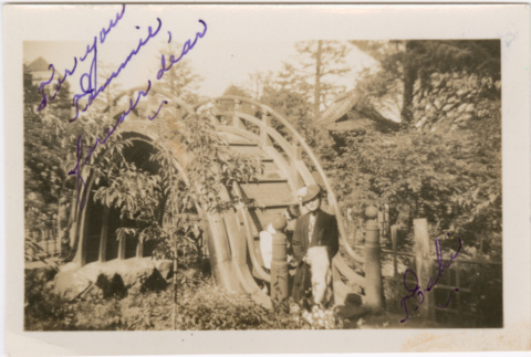 Tomoye (Nozawa) Takahashi standing by Moon bridge in garden (ddr-densho-426-1877)