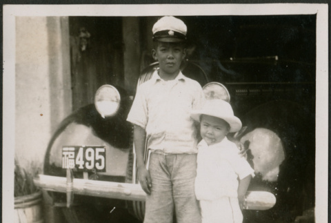 Two boys pose in front of a car (ddr-densho-359-952)