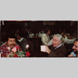 Three people at a table. Man at center holding box (ddr-densho-426-1261)