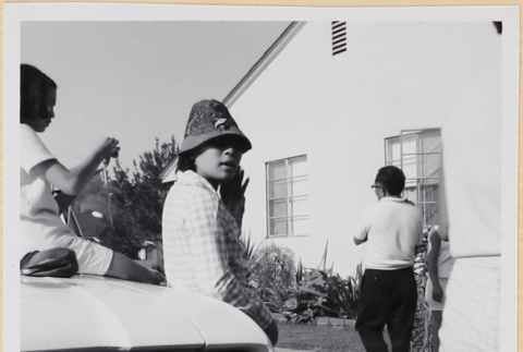 Woman in hat leaning on car in driveway (ddr-densho-522-95)