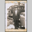 Man with glasses carrying a bag standing by row of cars (ddr-densho-483-993)