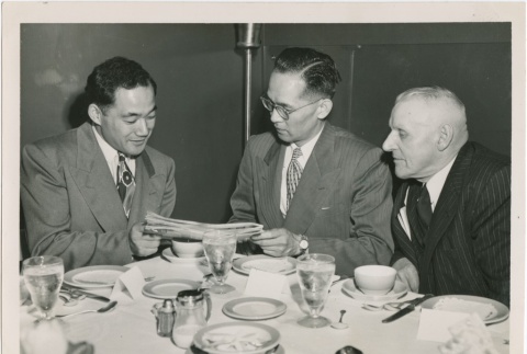 Three men looking at a newspaper (ddr-densho-296-94)