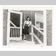 Sumi Seki wears a white shirt and plaid skirt while standing in front of barracks (ddr-csujad-52-45)