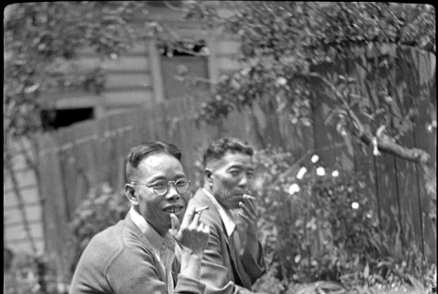 Two men sitting on a bench in garden, smoking (ddr-densho-426-1838)