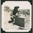 Walter Matsuoka squats next to a crate (ddr-densho-390-85)
