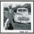 Photograph of an elderly man posing next to a car near the Manzanar hospital (ddr-csujad-47-259)
