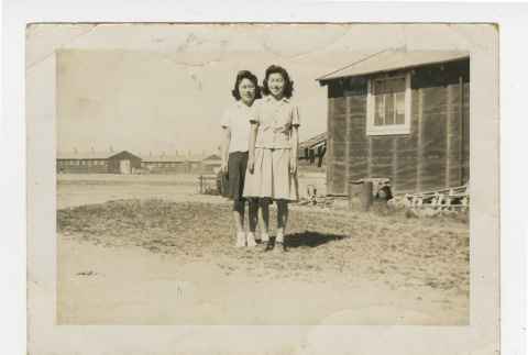 Nisei women standing outside with barracks in the background (ddr-csujad-44-7)