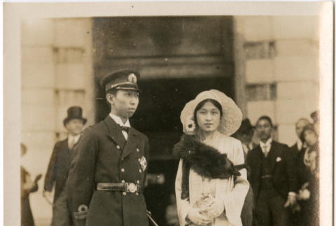 Woman wearing fur with man in uniform outside building (ddr-densho-426-2037)