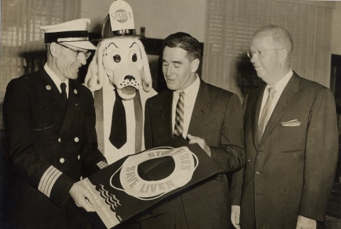 Naval officer, fire department mascot, Neal Blaisdell and another man with a poster (ddr-njpa-2-797)
