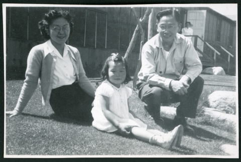 Photograph of Dr. and Mrs. Jiro Muramoto with daughter posing in front of the Manzanar hospital, with a nurse standing in the entrance (ddr-csujad-47-220)