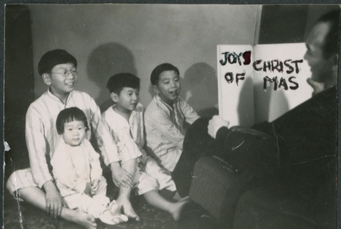 Staged holiday photo of Sakura children listening to Chester Sakura read from book titled: Joys of Christmas (ddr-densho-523-195)