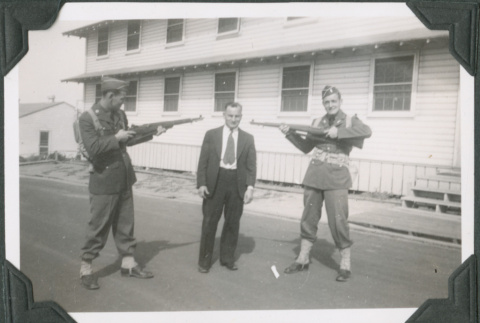 Two men in uniform jokingly pointing guns at third man in civilian clothes (ddr-ajah-2-127)