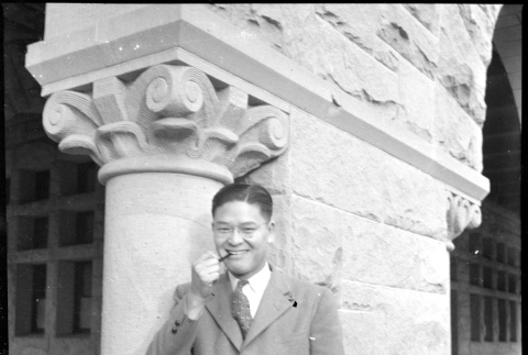 Man standing by carved stone pillar smoking a pipe (ddr-densho-426-2154)