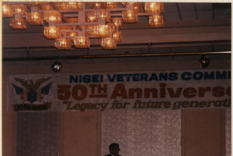 Man standing at podium under banner for 50th Anniversary Nisei Veterans Comm[...] (ddr-densho-466-551)