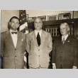 Three men posing in front of a bookcase and flag (ddr-njpa-2-697)