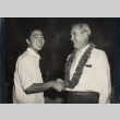 Young man shaking hands with a man wearing a lei (ddr-njpa-2-1027)