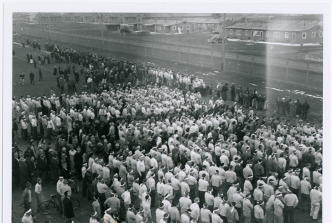 Large group of men wearing white headbands lined up along camp fence (ddr-densho-122-701)
