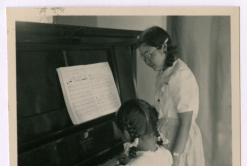Young girl plays piano her teacher observing (ddr-densho-362-24)