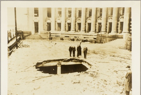 Men looking at a hole in the ground left by a bomb (ddr-njpa-13-250)