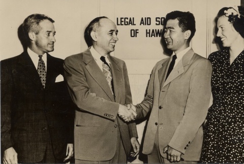 Two men shaking hands, posing with a woman and another man (ddr-njpa-2-948)