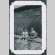 Two children on a bench with one in a baby walker outside barracks (ddr-densho-483-1096)