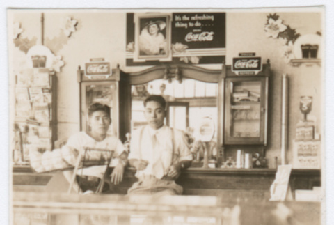 Two men behind drugstore counter (ddr-densho-383-390)
