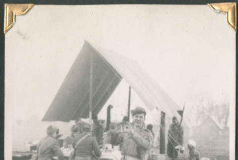 Man standing outside mess tent with men eating in background (ddr-densho-434-222)
