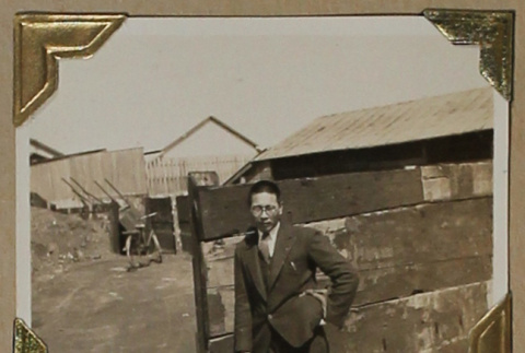 Man in a suit leans against a fence (ddr-densho-404-222)