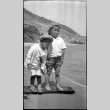 Two boys stand on a board on the beach (ddr-densho-480-24)