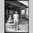 Joe Kuramoto in front of Asian-style building and fountain (ddr-densho-475-117)