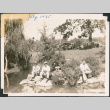 Three men sitting on rocks next to pond in Japanese Garden (ddr-densho-483-559)