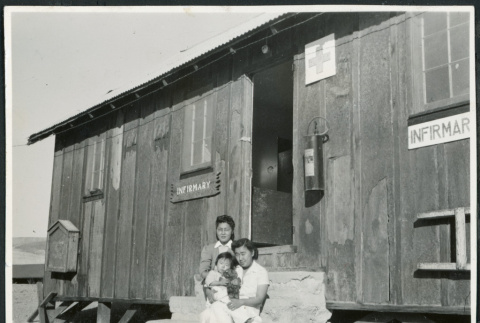 Photograph of two women an a young child posing in front of the infirmary at Cow Creek Camp in Death Valley (ddr-csujad-47-136)