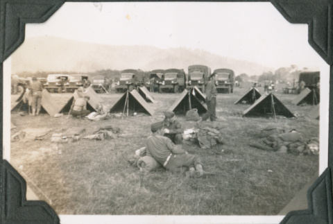Men resting outside row of tents with trucks in background (ddr-ajah-2-222)