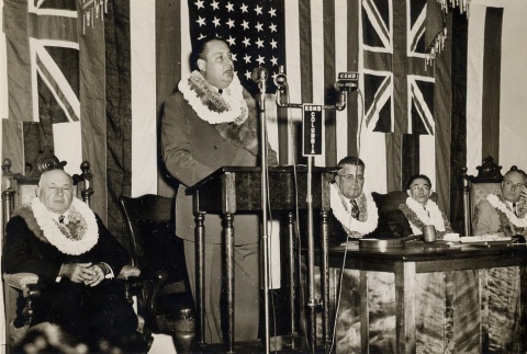 Man speaking at a podium, Ingram Stainback and other seated behind (ddr-njpa-2-1193)
