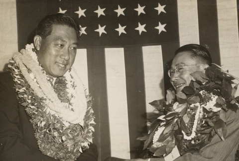 Two men wearing leis in front of a flag (ddr-njpa-2-303)