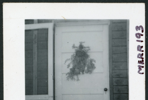 Photograph of a front door at Cow Creek Camp with a pine bough decoration (ddr-csujad-47-108)