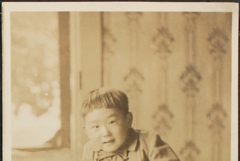 Nisei child sitting on a table with a statue (ddr-densho-259-155)