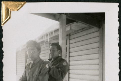 Two men sitting on railing, icicles on roof behind (ddr-densho-434-296)