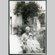 Photograph of Ned Morioka with his grandfather and cousin sitting on a bench with a house in the background (ddr-csujad-47-147)